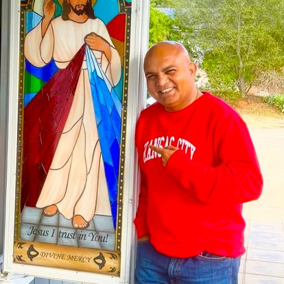 Un miembro de la comunidad junto a un vitral de la Divina Misericordia